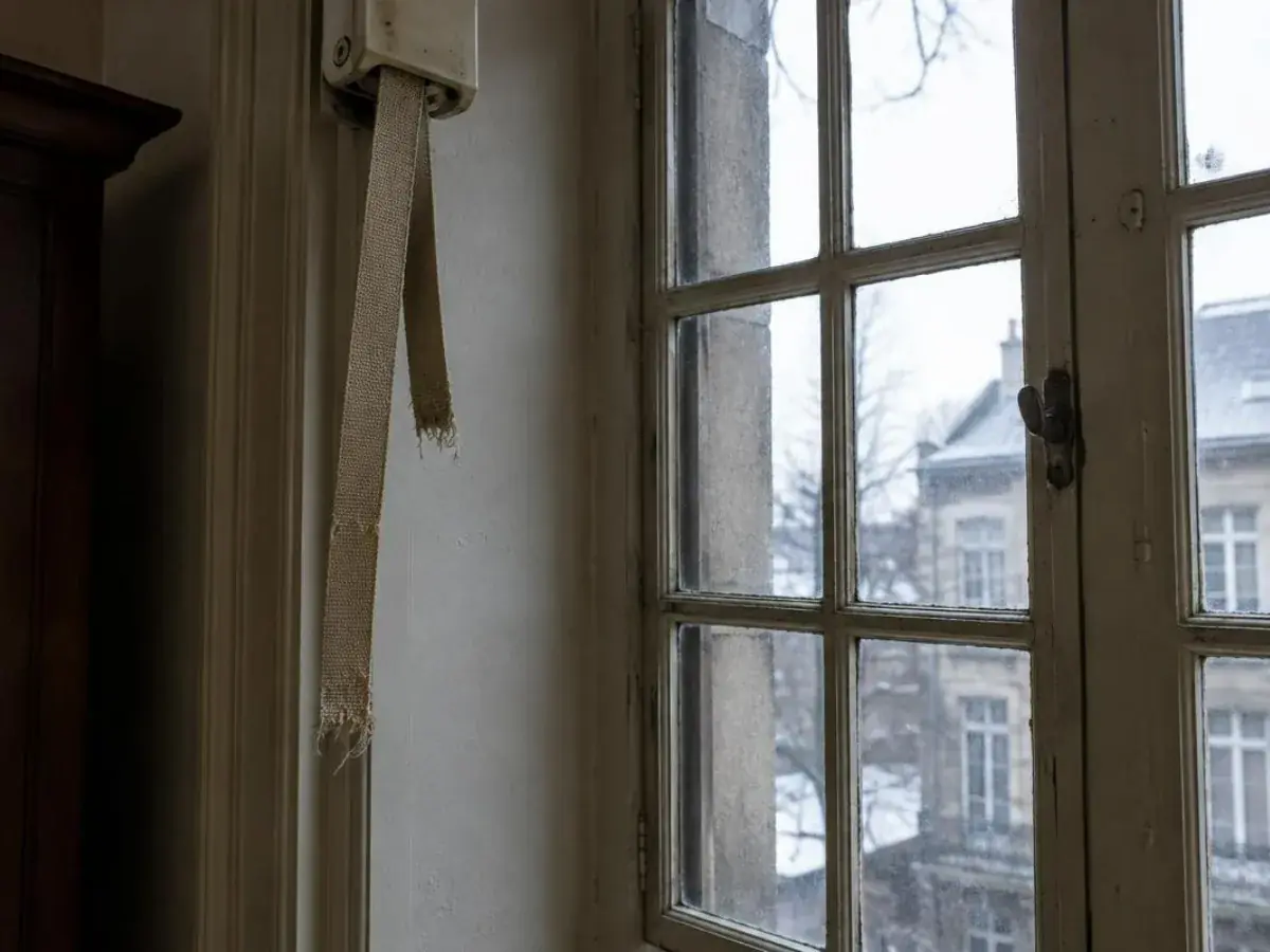 Main tenant une sangle de volet roulant déchirée devant son boîtier enrouleur encastré au mur